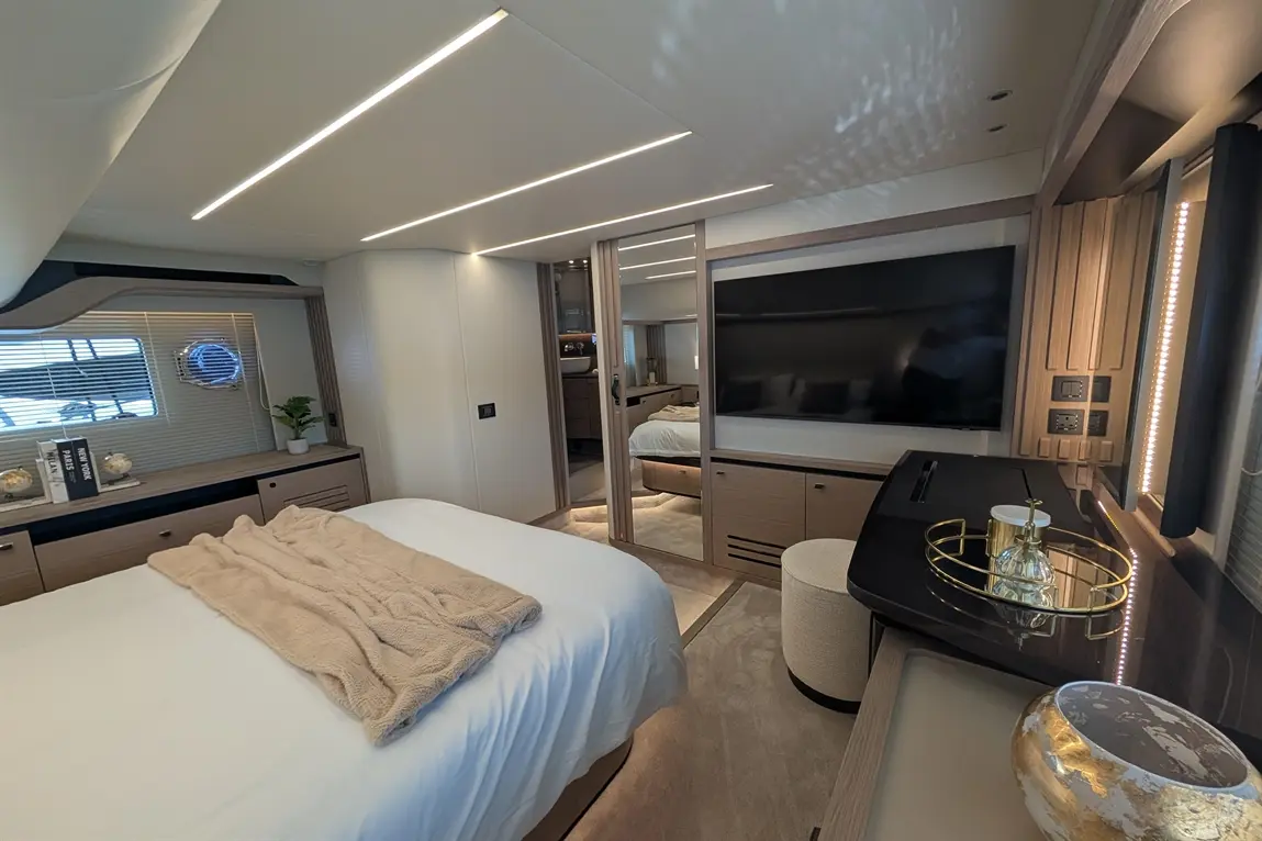 Modern bedroom featuring a large bed with a beige throw, sleek furniture, a TV, and stylish decor, illuminated by ambient lighting.